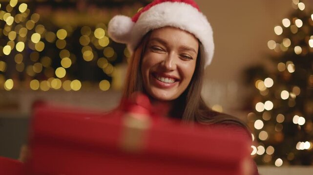 Woman in Santa hat joyfully reacting to Christmas gift and opening present