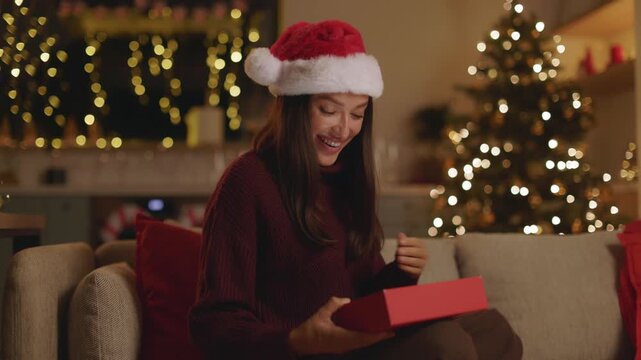 Excited woman in Santa hat opening Christmas gift box at home, 4K