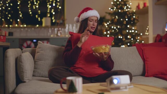 Tearful woman in Santa hat clutching red pillow, reacting to sad movie