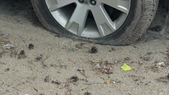 Flat car tire and wheel rim on dusty gravel ground with dirt buildup and visible damage