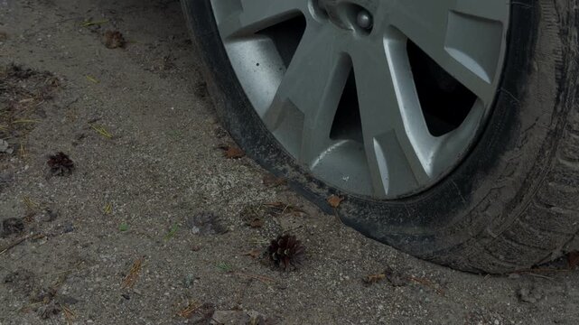 Flat car tire with damaged sidewall resting on gravel beside vehicle wheel and roadside debris