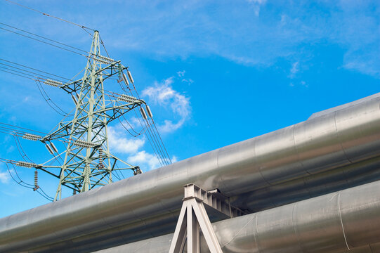 A close-up of a pipeline and a power transmission tower against a blue sky