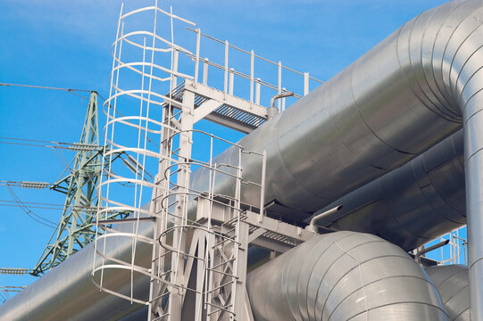 A close-up of a pipeline and a power transmission tower against a blue sky
