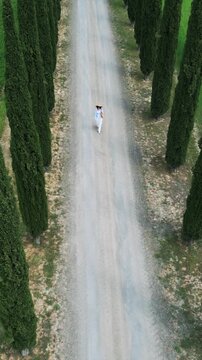 Woman move on a picturesque countryside road with cypress trees  in Tuscany, Italy