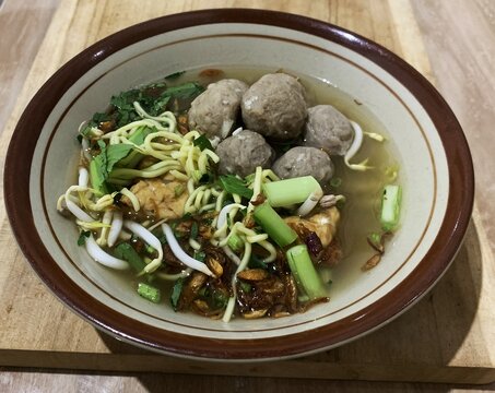 Indonesian meatball noodle soup ( bakso ) served in ceramic bowl on wooden table. savory broth.