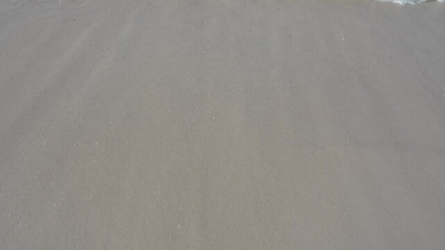 Close-up stock video footage of gentle ocean waves rolling in and receding over wet white sand beach, creating natural sea foam and delicate water ripples. Ideal for relaxation backgrounds, meditation