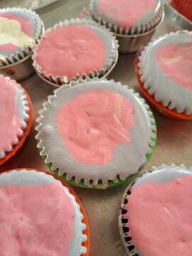 Overhead view of unbaked marble steamed cake batter in pink and gray swirls, sitting in metal molds ready for steaming. Bright bakery scene.