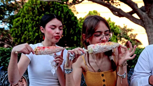 Mexican female friends eating elotes together outdoors