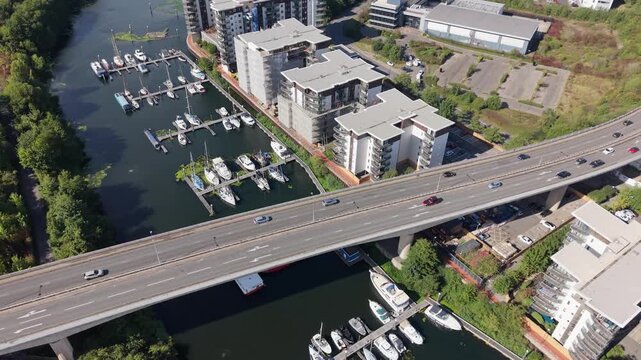Aerial drone flight over a busy road bridge near Cardiff, Wales, with moving traffic, moored boats, waterfront apartments and a marina visible alongside the water.