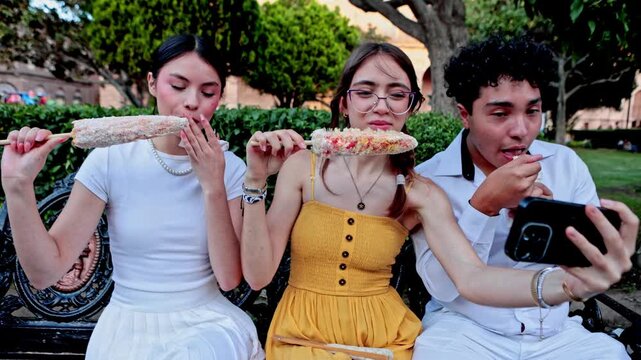 Mexican friends eating elote corn and taking selfie in a park