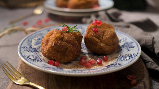 Sweet fried dough balls dusted with cinnamon and garnished with pomegranate seeds on a decorative plate