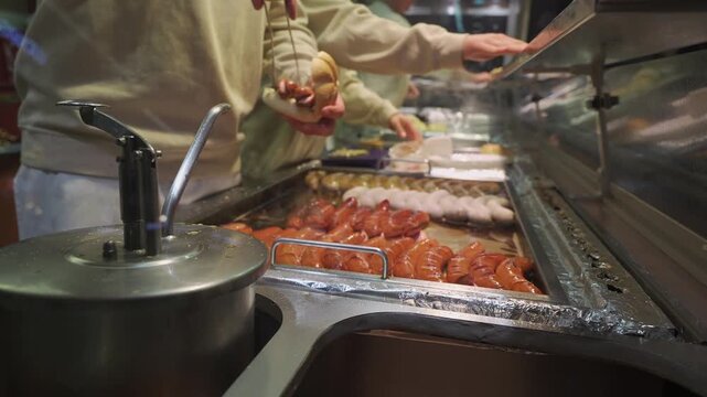 Street food at Munich Christmas fair with traditional German sausages. Chef hands preparing bratwurst, weisswurst, and currywurst in buns. Evening lights enhance festive mood.