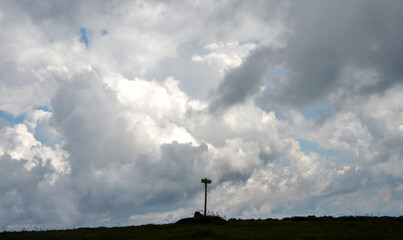 Solitary wooden directional signpost stands silhouetted atop a grassy hilltop beneath a vast, dramatic overcast sky filled with heavy grey and white clouds © Dmytro