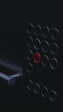 Vertical screen. Elevator control panel displays illuminated button for first floor, surrounded by various floor buttons and a metallic handle in a contemporary setting