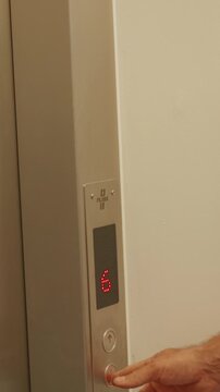 Vertical screen. Elevator control panel displays number six, finger pressing button, and downward arrow indicating elevator is moving downwards in a contemporary setting