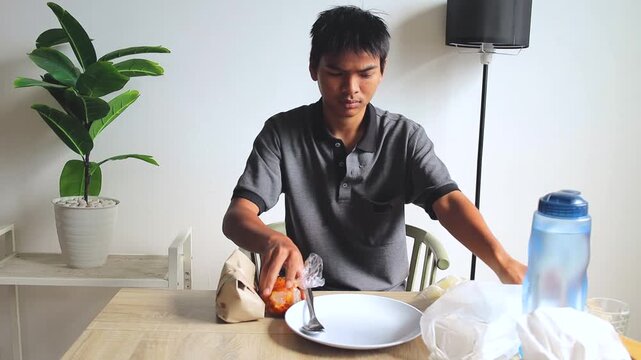 Young Asian man Unwrapping Wrapped meal tumeric rice packages at dining table 