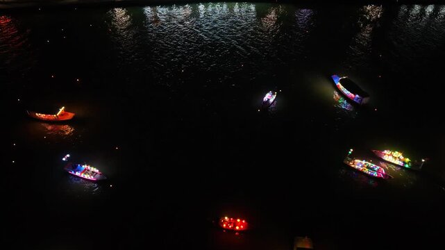Illuminated boats drift on the river at night in Hoi An, Vietnam, creating a beautiful display of colors and reflections on the water surface