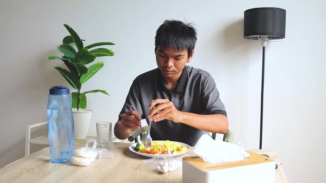 Young Asian man mixes turmeric rice with spicy egg and devours it at the dining table