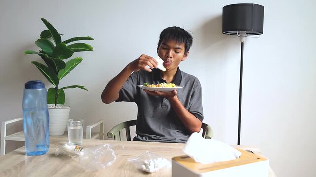 Young man Holding plate and eating crackers with spoon of rice during session of Eating Turmeric Rice at dining table