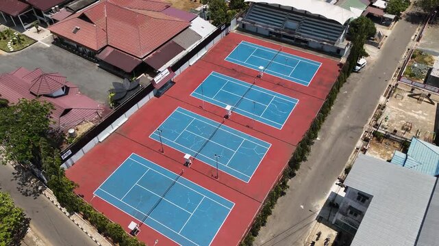Aerial perspective showing multiple tennis courts with blue surfaces and red borders outdoors