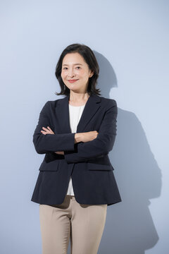 [水色背景]自信のある笑顔で立つ日本人ミドル女性、スーツ姿腕を組む50代の女性ビジネスパーソンカメラ目線笑顔上半身