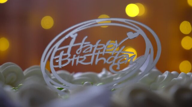 Happy Birthday text. Birthday cake with white cream cheese, cake tier. Delicate lambeth style birthday cake with white cream cheese, festive background with string lights.