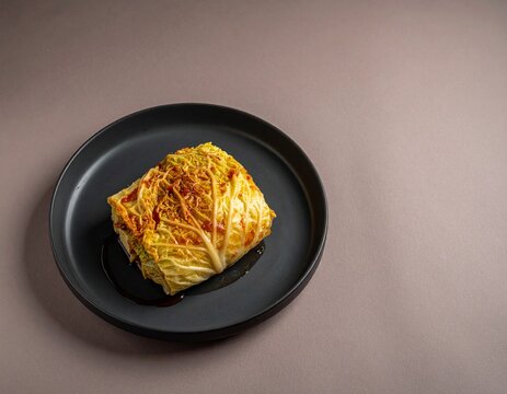 Baked stuffed cabbage roll with melted cheese on black ceramic plate on light pink background