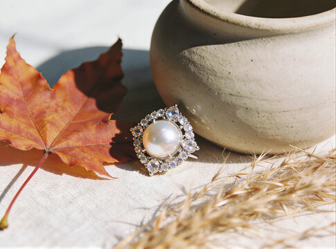 Pearl ring with a gemstone halo on linen beside an autumn maple leaf