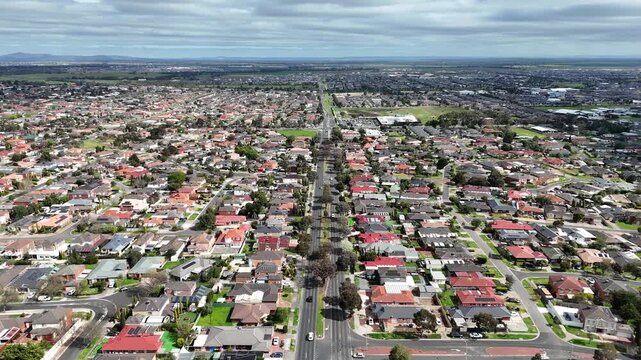 Aerial drone view of a main road stretching through Hoppers Crossing toward Tarneit, with dense suburban rooftops and distant urban sprawl. Melbourne, Victoria, Australia. Western suburban expansion 