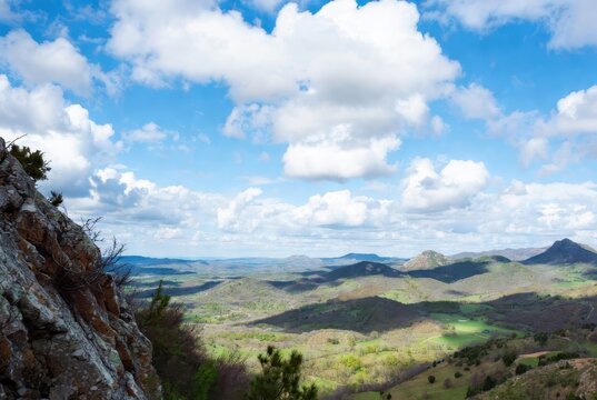 Panoramic mountain valley with rocky cliff, rolling green hills and expansive cloud filled blue sky