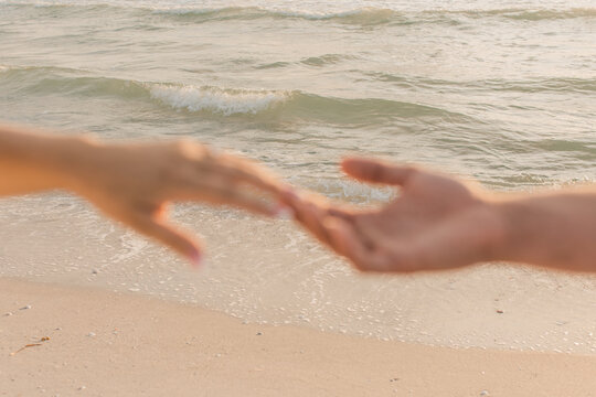 man and woman holding hands against the ocean beach shore water waves 