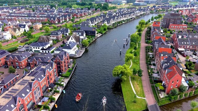 Wide horizontal aerial drone video of residential canal district, small motorboats, modern waterfront townhouses, solar roofs, and green park paths in Leiden, South Holland, Netherlands