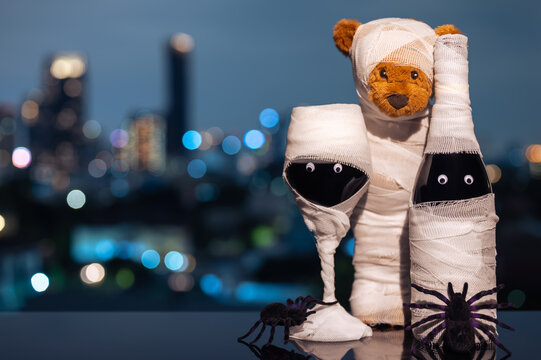 Halloween mummy bear, wine bottle, and glass with spiders against a city skyline at night.