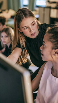 Mentorship in Action: Two young women collaborate at a computer, with one guiding the other, embodying the spirit of learning and knowledge transfer.