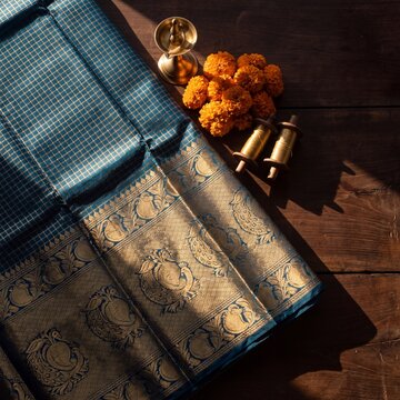 Teal Silk Saree with Gold Zari Peacock Border, Brass Lamp and Marigold Flowers on Wooden Table