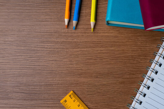 Flat lay of office stationery with colored pencils, notebooks and ruler with copy space on a wooden desk. Back to school, education, workplace, productivity and planning concept.