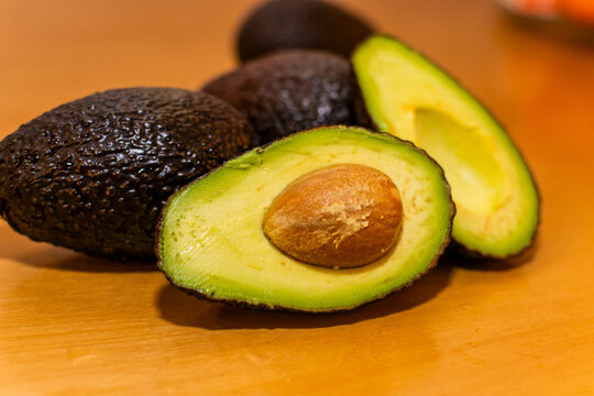 Primer plano centrado en dos mitades de aguacate fresco con aguacates enteros detr&aacute;s, desenfocados, sobre mesa madera
