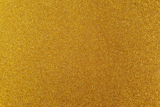 Macro texture of fine gold glitter surface with subtle shimmering particles. Seamless abstract background.