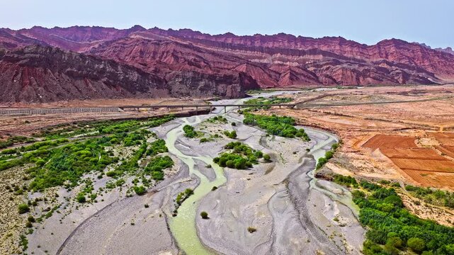 Aerial view of a riverbed winding through a red rock mountain valley with a bridge in Xinjiang, China