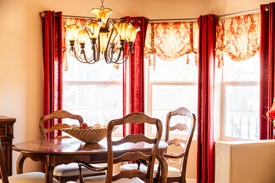 Chandelier over round wooden dining table in elegant dining room with red drapes and golden daylight