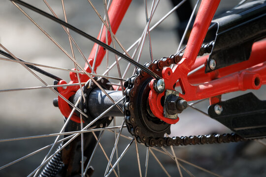 detailed close-up shot focusing on the rear hub assembly and drivetrain mechanics of a bright orange-red bicycle frame, drive chain wrapped around a single rear sprocket, black central hub axle