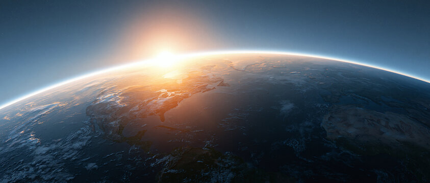 A beautiful bright sun rising over the curved horizon of the planet earth seen from deep space with a dark blue atmosphere above the globe