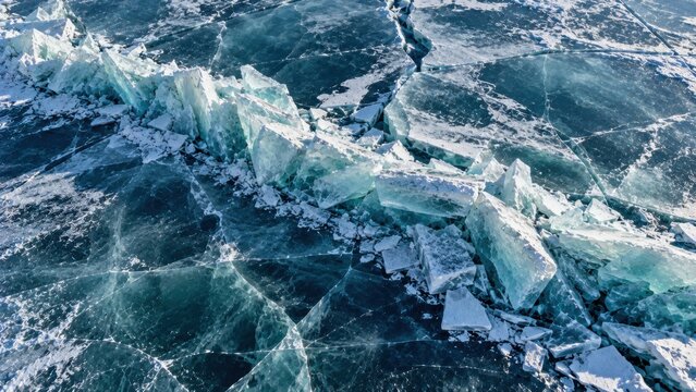 Pressure ridge in clear lake ice, uplifted turquoise slabs, radiating fractures and dark frozen surface. Winter texture background for design. For climate media and seasonal publishing.