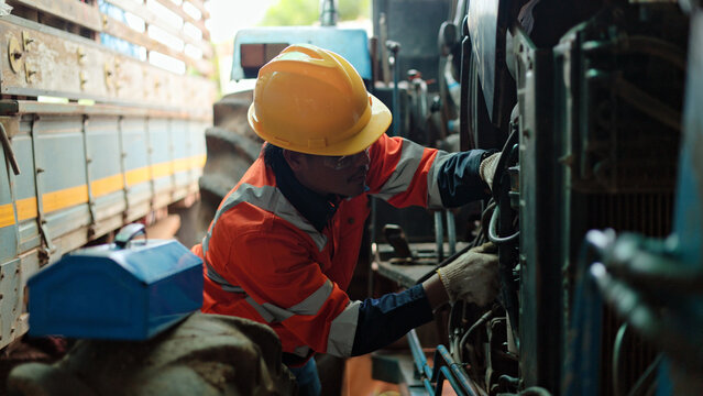 Professional mechanic inspecting and repairing engine of heavy agricultural tractor, farm equipment maintenance and repair service concept.
