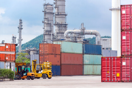 Yellow forklifts working in cargo container yard with oil refinery plant background. Global shipping logistics. Human-created, not AI.