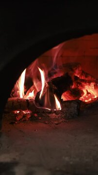 Vertical video. Fire stove. Kitchen oven. Wood burning in old arch brick furnace. Glowing red orange roaring flame on ash black logs.