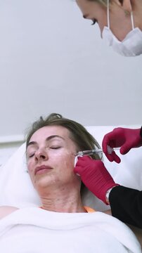 Vertical video. Cosmetic injection. Woman procedure. Cosmetologist in gloves using dermal filler for face medical treatment in beauty clinic.