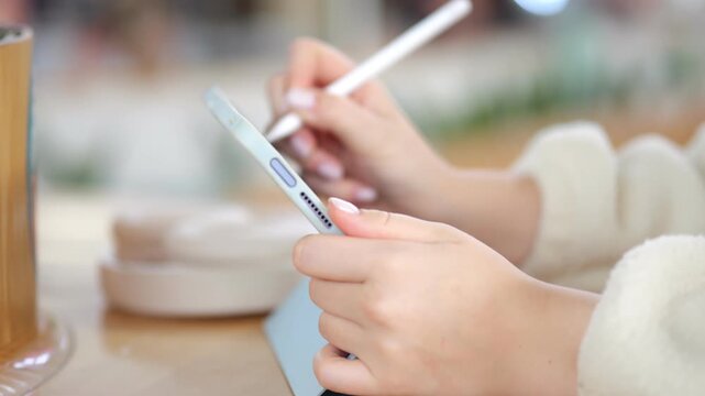 Hands use stylus on tablet in cafe. Wooden cup and saucer nearby. Soft focus background. Light natural tones. Casual indoor setting. Focus on creative work