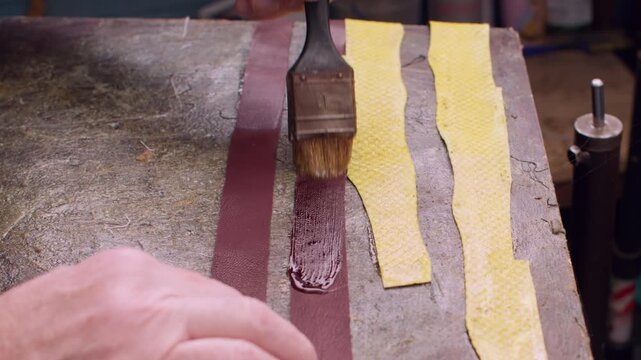 Tailor occupation. Shoemaker craft. Professional craftsman hands using brush applying glue on red yellow color fabric material.