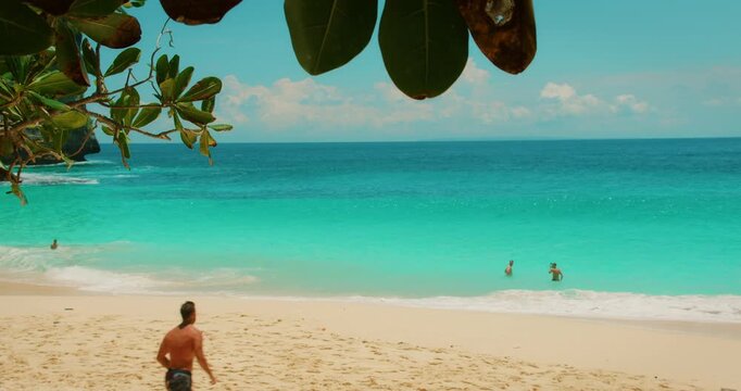 Young men running into turquoise ocean water at Kelingking Beach in Nusa Penida Bali